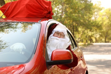 Authentic Santa Claus with bag full of presents on roof driving modern car, outdoors