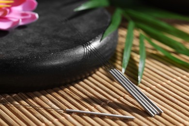 Acupuncture needles and spa stone on bamboo mat, closeup