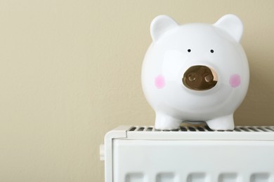 Photo of Piggy bank on heating radiator against beige background, space for text