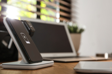 Photo of Mobile phone and smartwatch charging with wireless pad on wooden desk, space for text. Modern workplace device