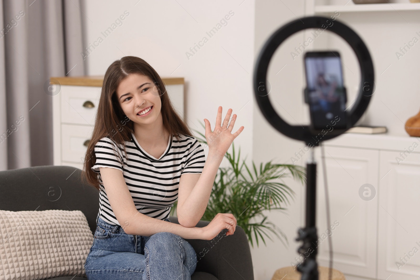 Photo of Smiling teenage blogger waving hello to her subscribers while streaming at home