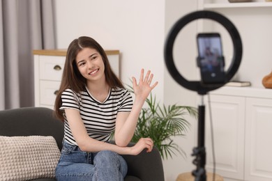 Smiling teenage blogger waving hello to her subscribers while streaming at home