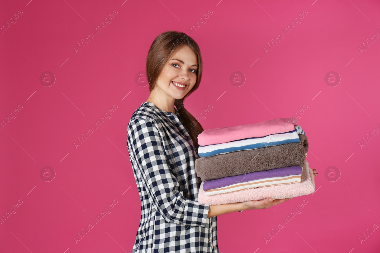 Photo of Happy young woman holding clean laundry on color background