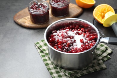 Photo of Making cranberry sauce. Fresh cranberries with sugar in saucepan and ingredients on gray table, space for text