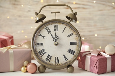 Photo of Vintage alarm clock with decor on white table against blurred Christmas lights, closeup. New Year countdown