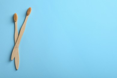 Photo of Two bamboo toothbrushes on light blue background, flat lay. Space for text