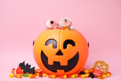 Photo of Halloween trick or treat bucket with different sweets on pink background