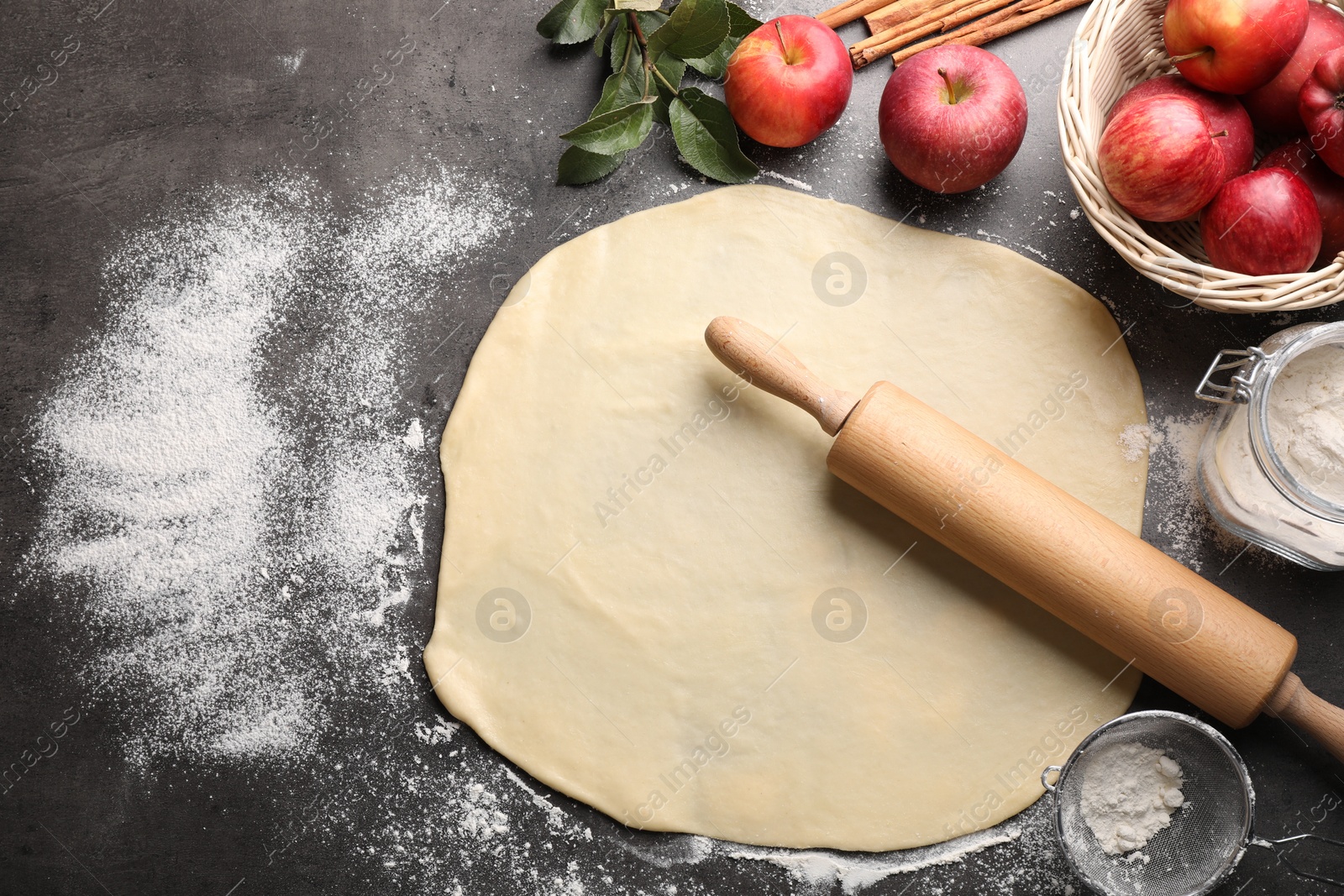Photo of Fresh dough, rolling pin, ingredients and leaves on grey table, flat lay. Making apple pie