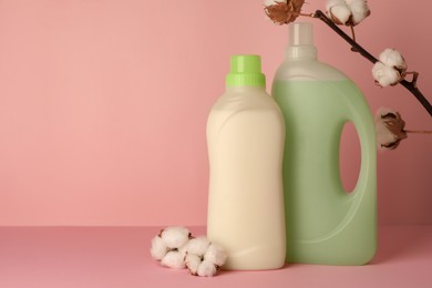 Photo of Bottles of fabric softener and fluffy cotton flowers on pink background, space for text