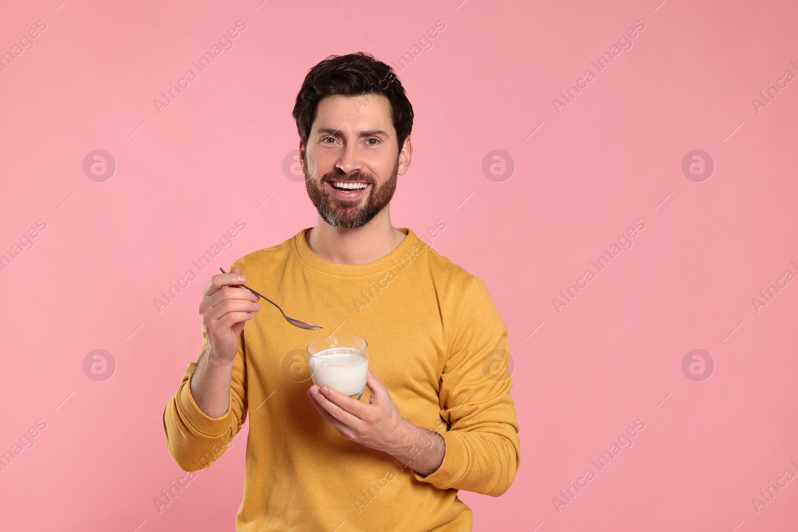 Photo of Handsome man with delicious yogurt and spoon on pink background. Space for text