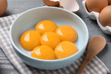 Photo of Bowl with raw egg yolks on grey wooden table, closeup