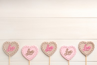 Photo of Different chocolate heart shaped lollipops with word Love on white wooden table, flat lay. Space for text