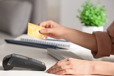 Woman using modern payment terminal at table indoors, closeup