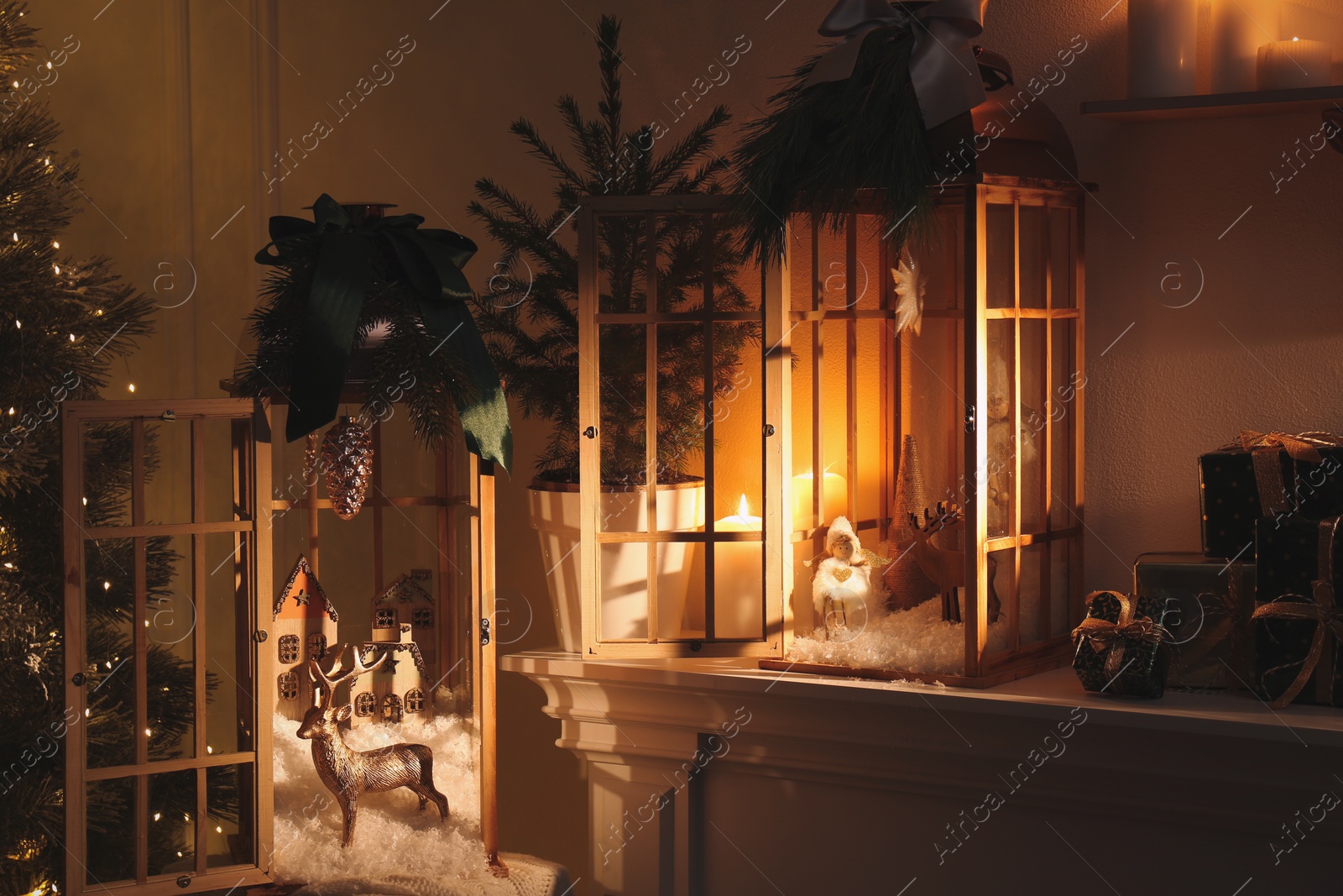 Photo of Beautiful wooden lanterns and other decorations on mantelpiece in room with Christmas tree