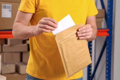 Photo of Post office worker putting envelope into adhesive bag indoors, closeup