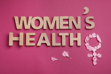 Photo of Words Woman's Health and female gender sign made of petals on dark pink background, flat lay