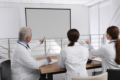 Photo of Team of doctors using video projector during conference indoors