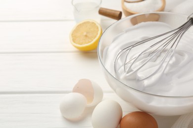 Photo of Bowl with whipped cream, whisk and ingredients on white wooden table. Space for text