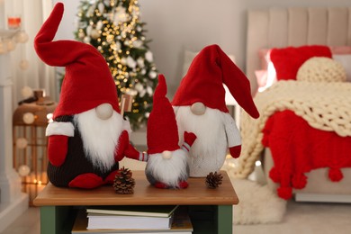 Photo of Cute Christmas gnomes on wooden table in room with festive decorations