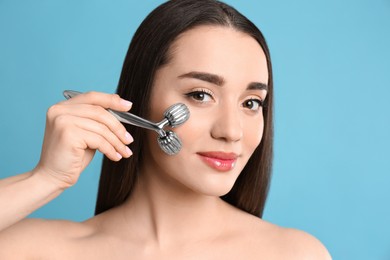 Woman using metal face roller on light grey  background
