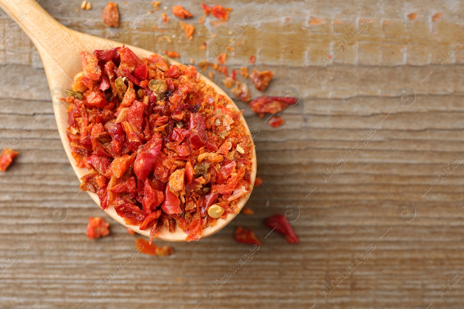 Photo of Aromatic spice. Red chili pepper flakes in spoon on wooden table, top view. Space for text