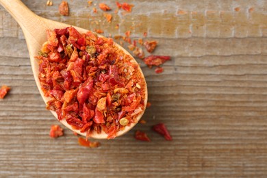 Photo of Aromatic spice. Red chili pepper flakes in spoon on wooden table, top view. Space for text