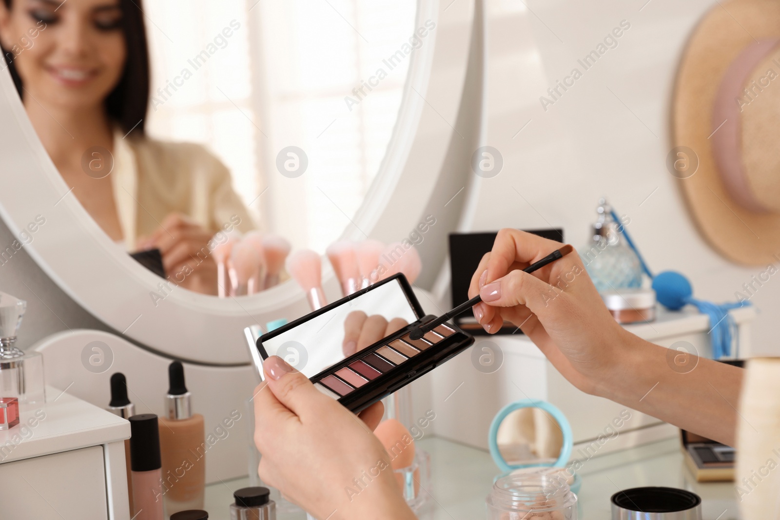 Photo of Beautiful young woman applying makeup near mirror indoors, closeup