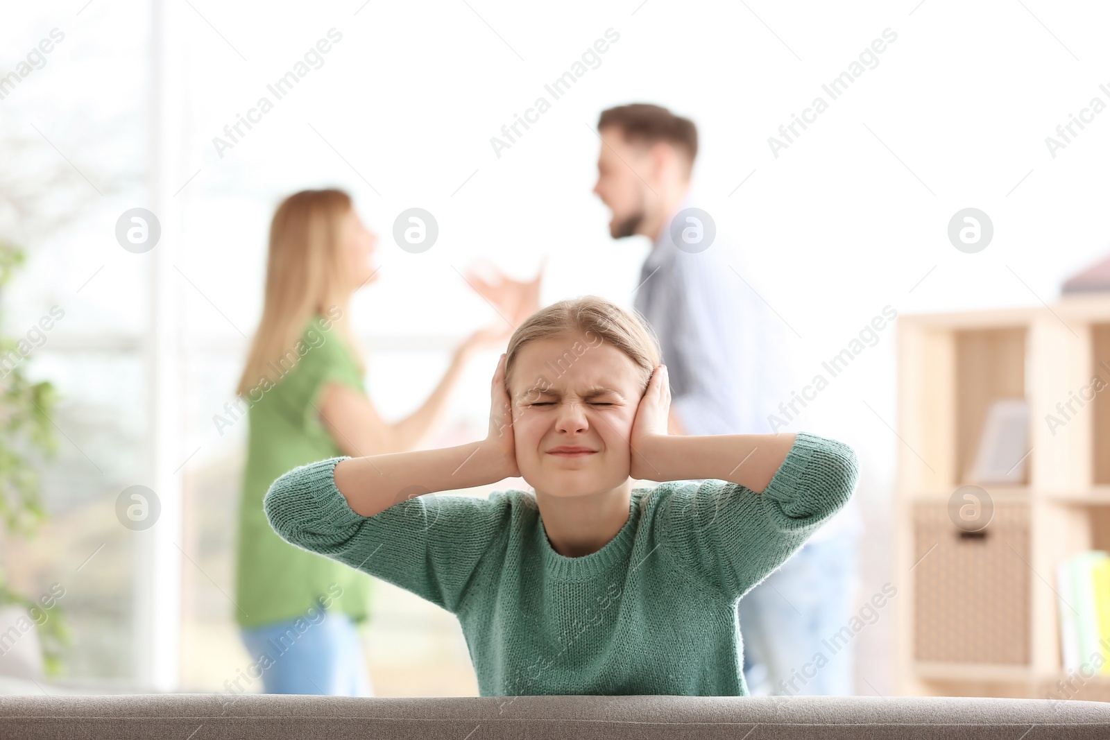 Photo of Little unhappy girl sitting on sofa while parents arguing at home