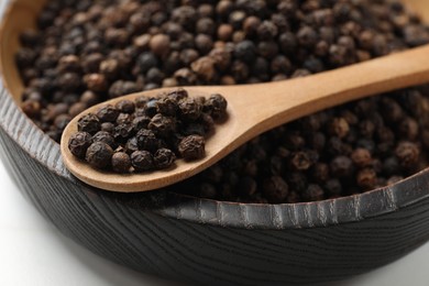 Photo of Aromatic spice. Black pepper in bowl and spoon on white table, closeup