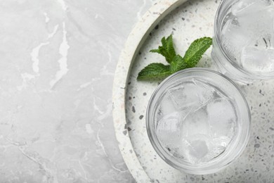 Photo of Glasses of soda water with ice and mint on grey table, top view. Space for text
