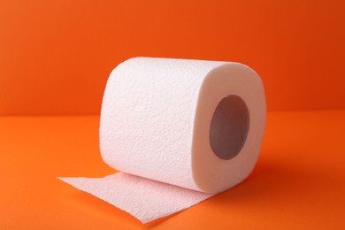 Photo of Soft toilet paper roll on orange background, closeup