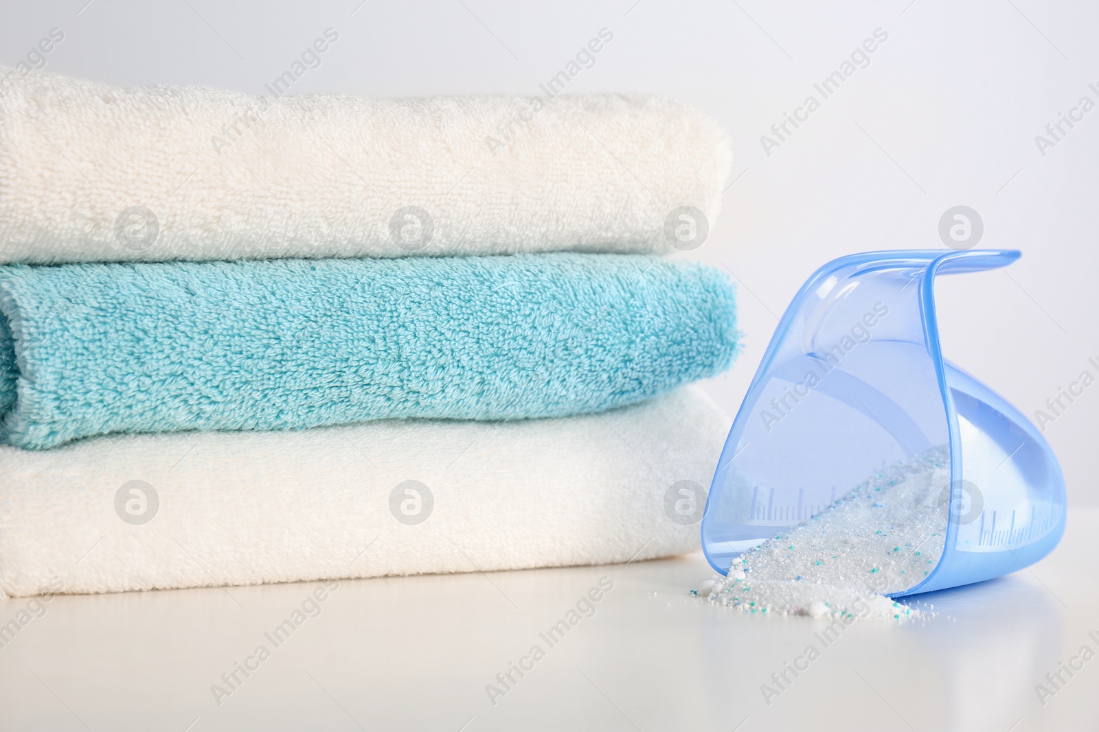 Photo of Measuring cup with washing powder and clean towels on white background. Laundry day