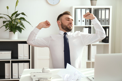 Photo of Lazy young man stretching at messy table in office