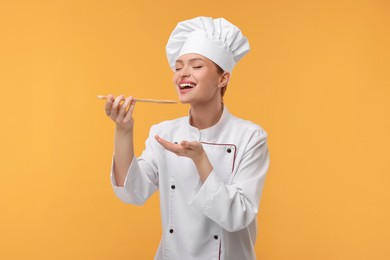 Happy chef in uniform tasting something on orange background