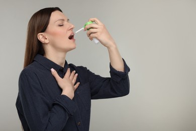 Photo of Woman using throat spray on grey background, space for text