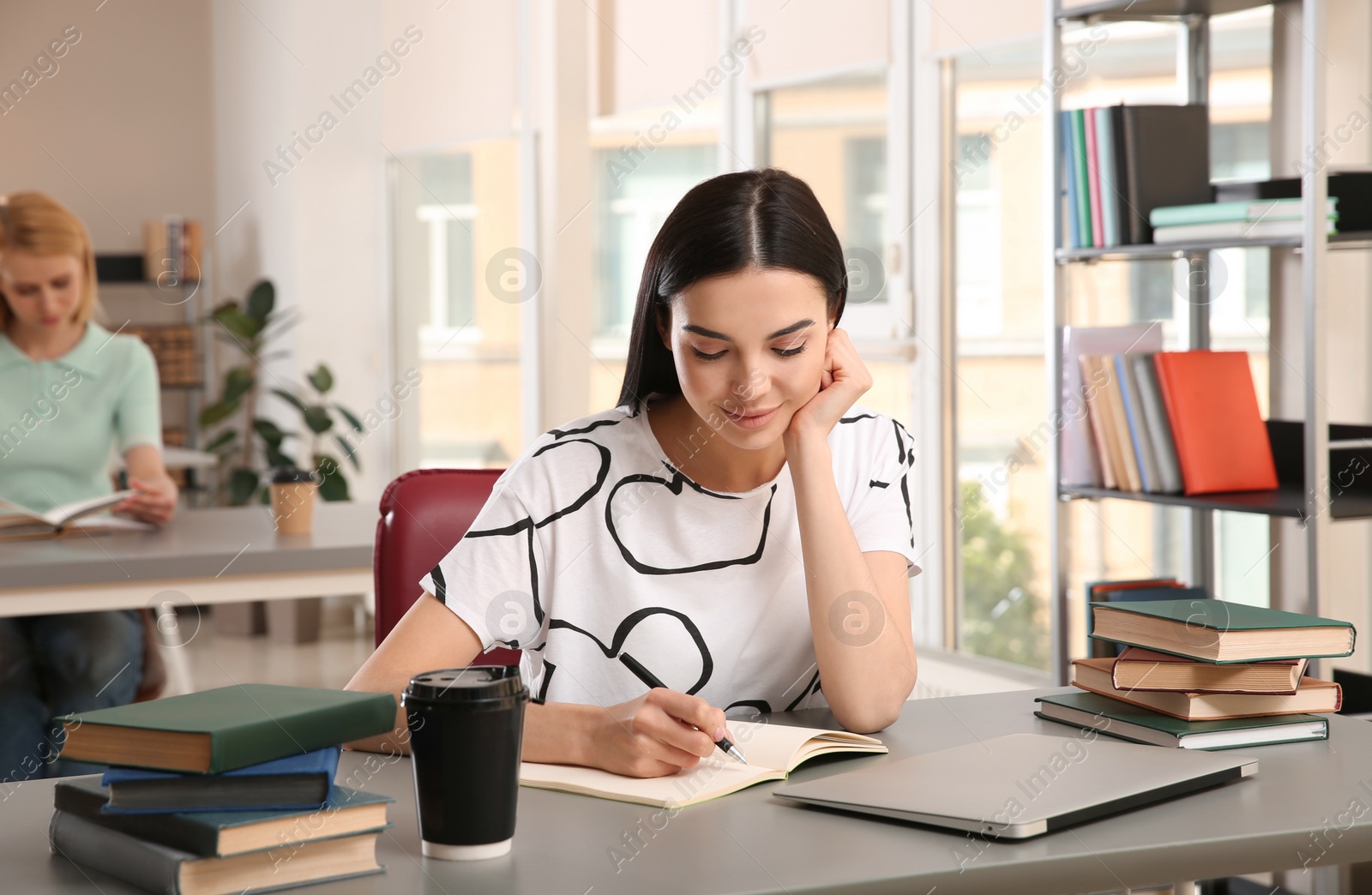 Photo of Young woman studying at table in library