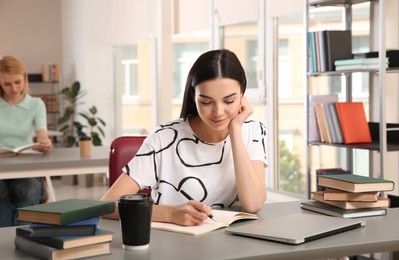 Photo of Young woman studying at table in library