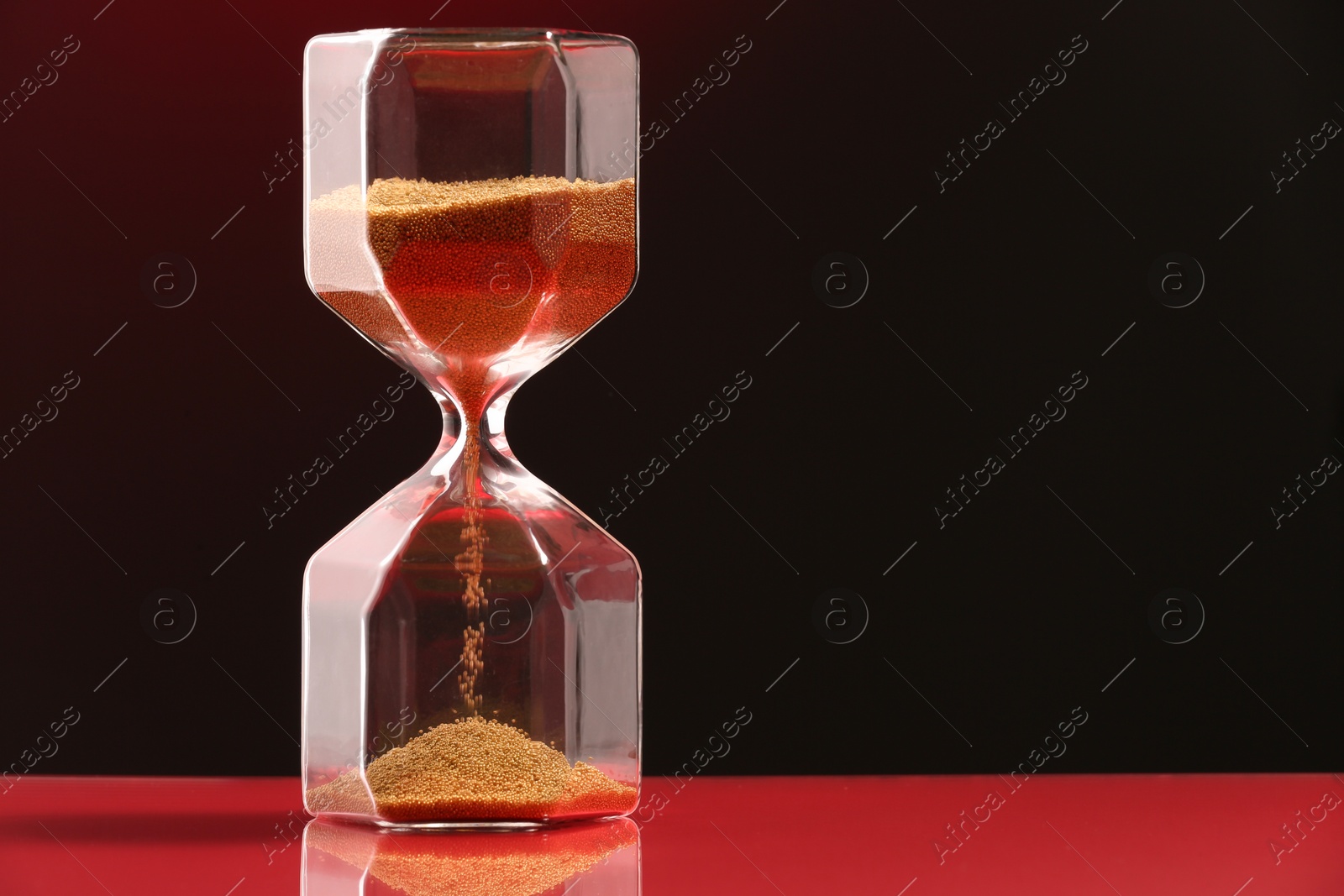 Photo of Hourglass with flowing sand on table against dark background. Space for text