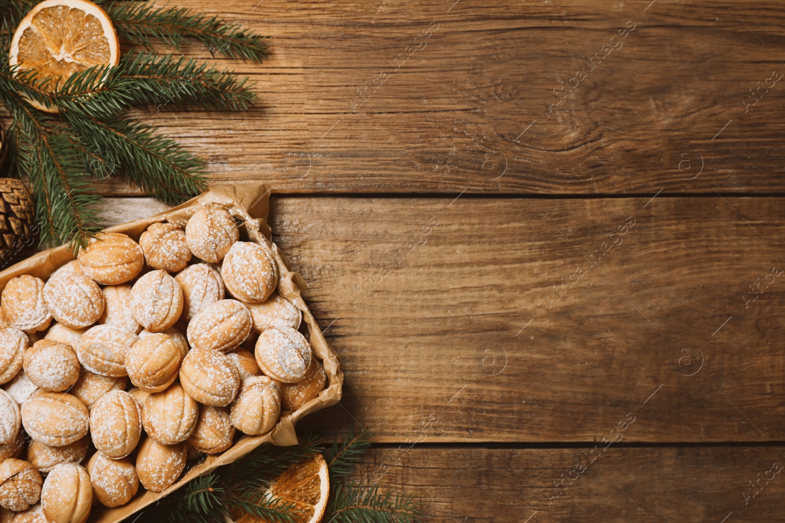 Photo of Delicious nut shaped cookies with boiled condensed milk, dry orange slices and fir tree branches on wooden table, flat lay. Space for text