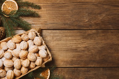 Delicious nut shaped cookies with boiled condensed milk, dry orange slices and fir tree branches on wooden table, flat lay. Space for text