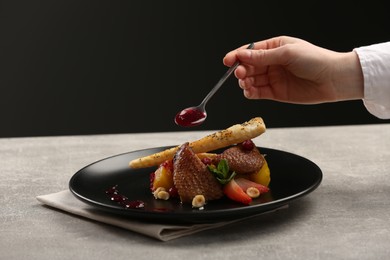 Photo of Food stylist adding sauce to delicious dish with chicken, parsnip and strawberries for photoshoot at grey table in studio, closeup