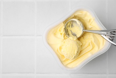 Photo of Vanilla ice cream and scoop in container on white tiled table, top view. Space for text