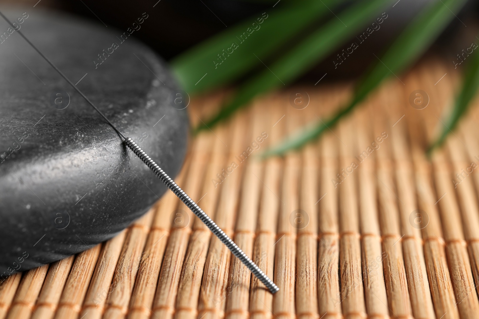 Photo of Acupuncture needle and spa stone on bamboo mat, closeup. Space for text