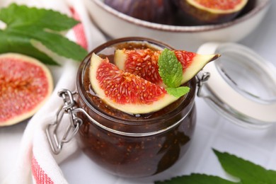 Glass jar of tasty sweet fig jam and fruits on table, closeup