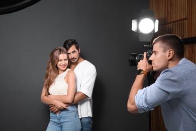 Photo of Professional photographer taking picture of young couple on dark grey background in modern studio