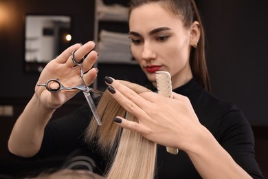 Photo of Professional hairdresser cutting woman's hair in salon, focus on hands