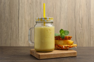 Tasty pineapple smoothie and sliced fruit on wooden table
