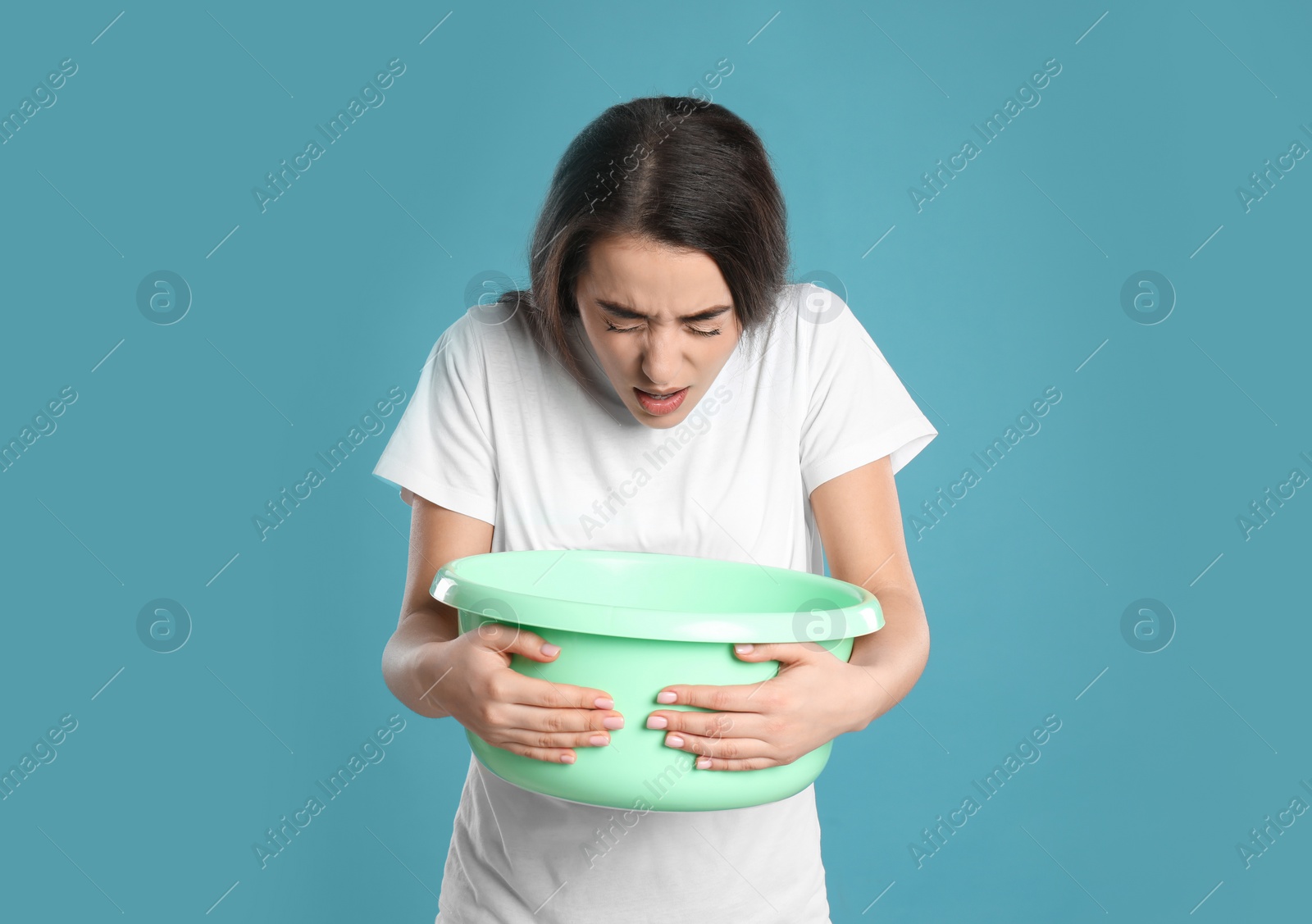 Photo of Young woman with basin suffering from nausea on light blue background. Food poisoning