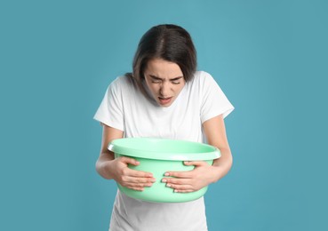 Young woman with basin suffering from nausea on light blue background. Food poisoning