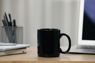 Photo of Black ceramic mug, notebooks and laptop on wooden table at workplace